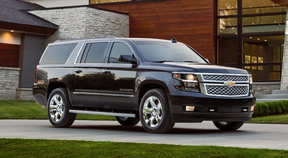 Black 2018 Chevrolet Suburban parked in front of a brown wood and grey stone house