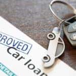 Car key with a car keychain attached sitting on top of an approved car loan application