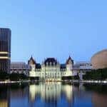 NY state building next to tall Albany, NY buildings with water in front of it
