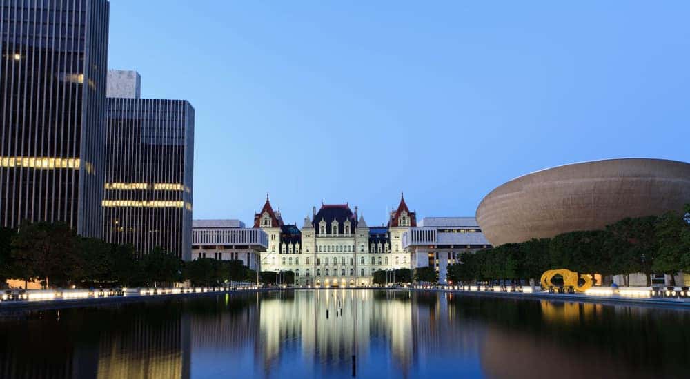 NY state building next to tall Albany, NY buildings with water in front of it