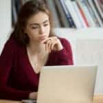 Woman in a maroon sweater sitting at a brown desk using a silver laptop