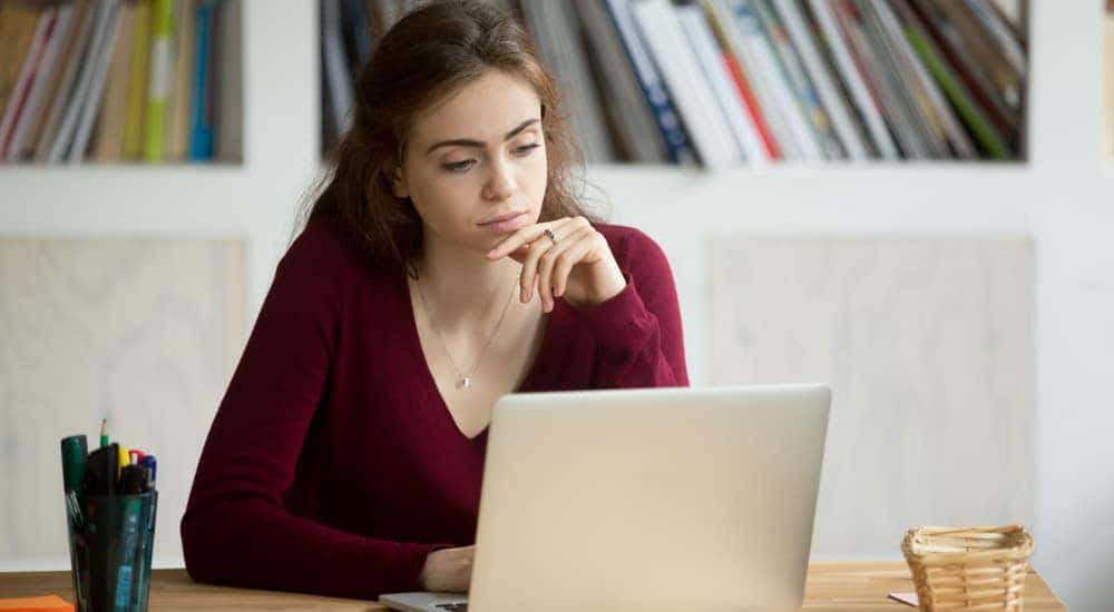 Woman in a maroon sweater sitting at a brown desk using a silver laptop