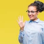 Woman in a blue button-up holding five fingers up in front of a yellow wall