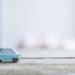 Small, light blue toy car sitting on a light grey table