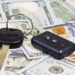 Black car key and fob laying on a pile of one-hundred dollar bills