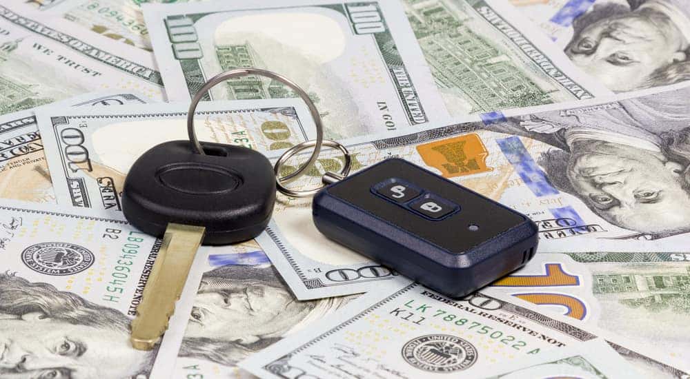 Black car key and fob laying on a pile of one-hundred dollar bills