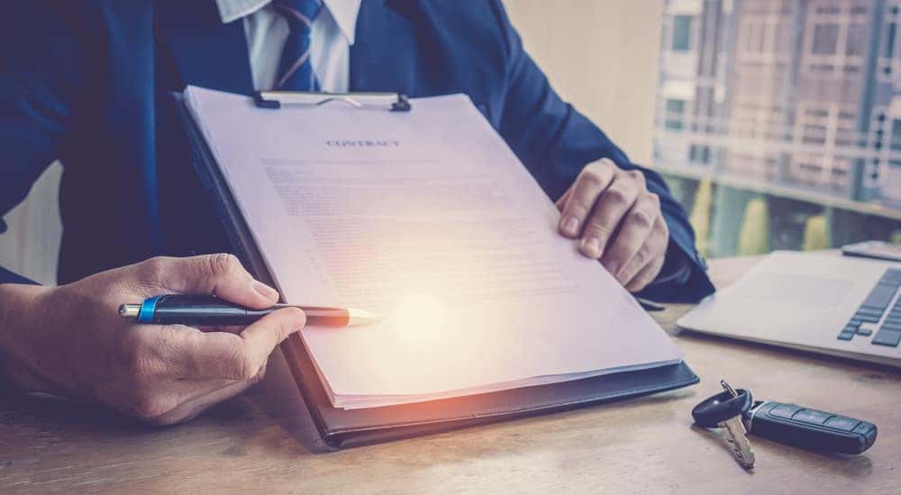 Man in a suit holding up a contract on a clipboard on a desk with car keys sitting on it