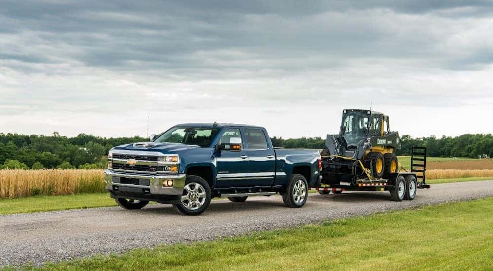Blue 2018 Chevrolet Silverado 2500HD driving down a paved road pulling construction equipment on a trailer