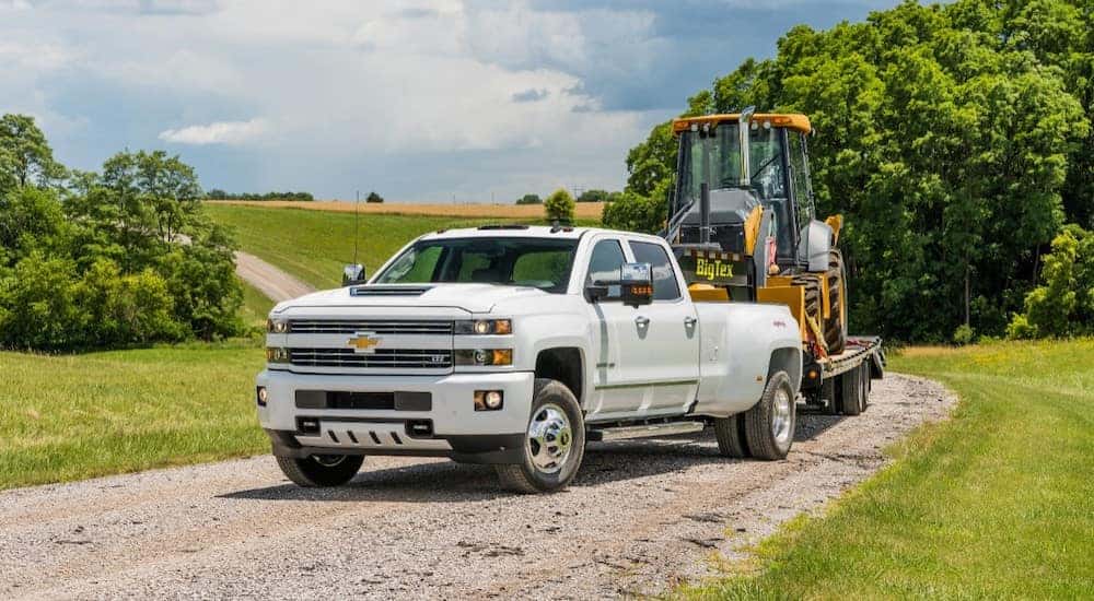 White 2018 Chevrolet Silverado 3500HD pull construction equipment down a dirt road