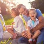 Laughing family sitting on a blanket in a field on a sunny day