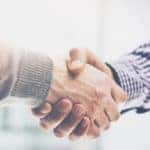 Handshake between an arm in a plaid shirt and an arm in a grey sweater