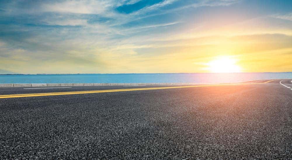 Paved road running parallel to a body of water with a summer sunset in the background