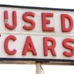 White sign with a black border and "USED CARS" written on it in red