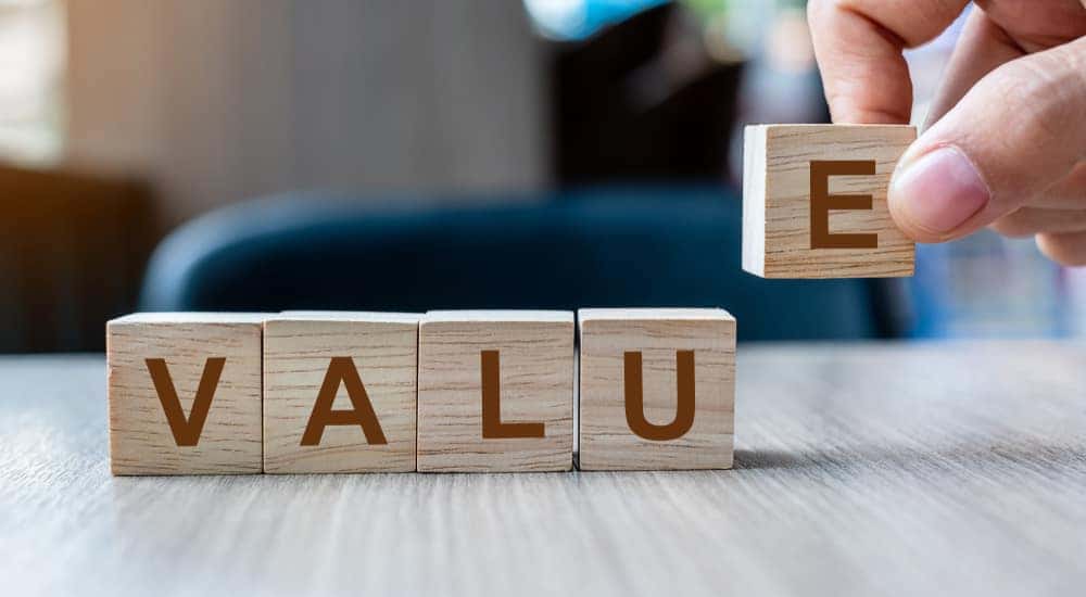 Hand placing an "E" letter block on a grey table next to other blocks to spell out the word "VALUE"