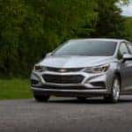 Silver 2018 Chevrolet Cruze driving down a paved road next to green grass and trees