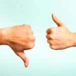 One thumbs down and one thumbs up, coming from opposite sides, in front of a blue wall