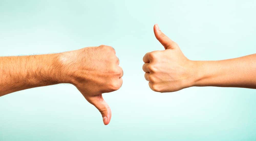 One thumbs down and one thumbs up, coming from opposite sides, in front of a blue wall