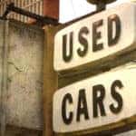Vintage "USED CARS" sign hanging off a cement building