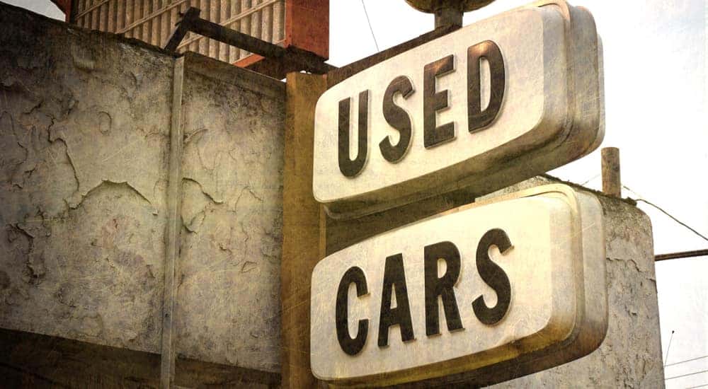 Vintage "USED CARS" sign hanging off a cement building