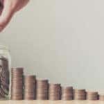 Ten consecutively taller stacks of coins leading up to a jar of coins in which a hand is placing another coin in