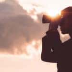 Silhouette of a man looking through binoculars with pink clouds behind him