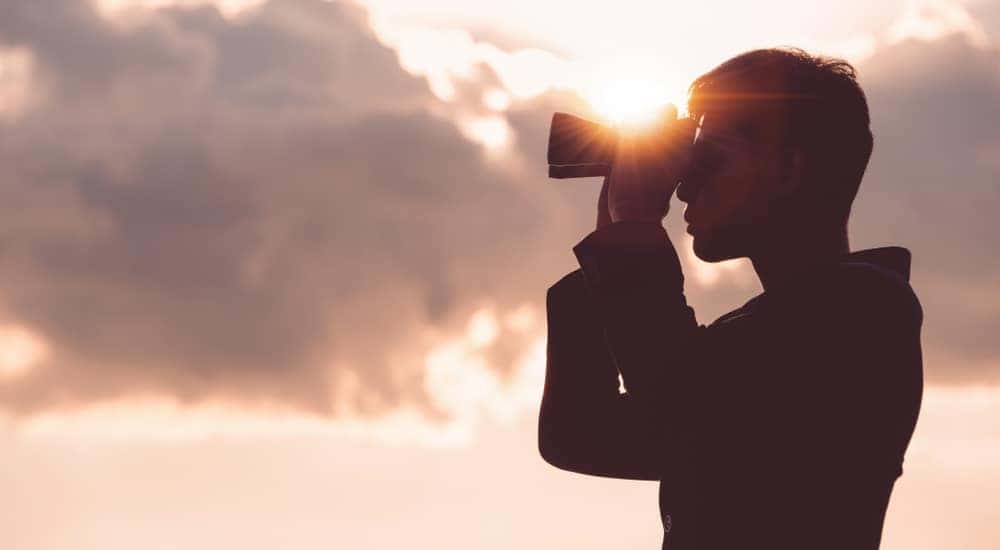 Silhouette of a man looking through binoculars with pink clouds behind him