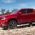 Red 2018 Chevrolet Colorado pickup truck driving down a dirt hill in front of trees