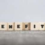 Light wood blocks that spell out "BENEFITS" sitting on a dark table