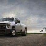 White 2020 Chevrolet Silverado 3500HD truck parked on a dirt path with a dark sky and white barn in the background