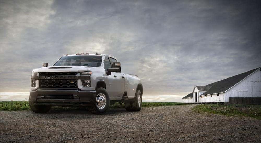 White 2020 Chevrolet Silverado 3500HD truck parked on a dirt path with a dark sky and white barn in the background
