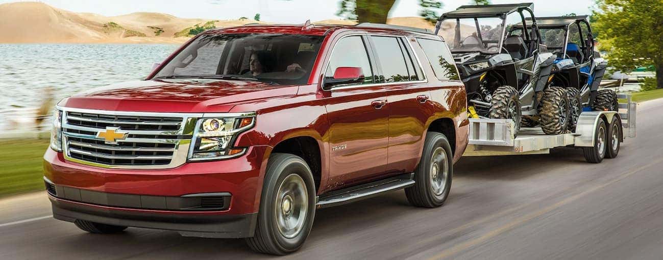 A red 2020 Chevy Tahoe is towing a trailer with 2 side by sides on it.