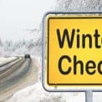 A winter check sign is shown in front of a snow covered road in Albany, NY.
