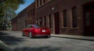 A red 2017 Chevy Malibu is driving past an old brick building near Albany, NY.