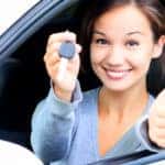 Teen girl sitting in the driver's seat of a white vehicle with the window open holding up a car key and a thumbs up