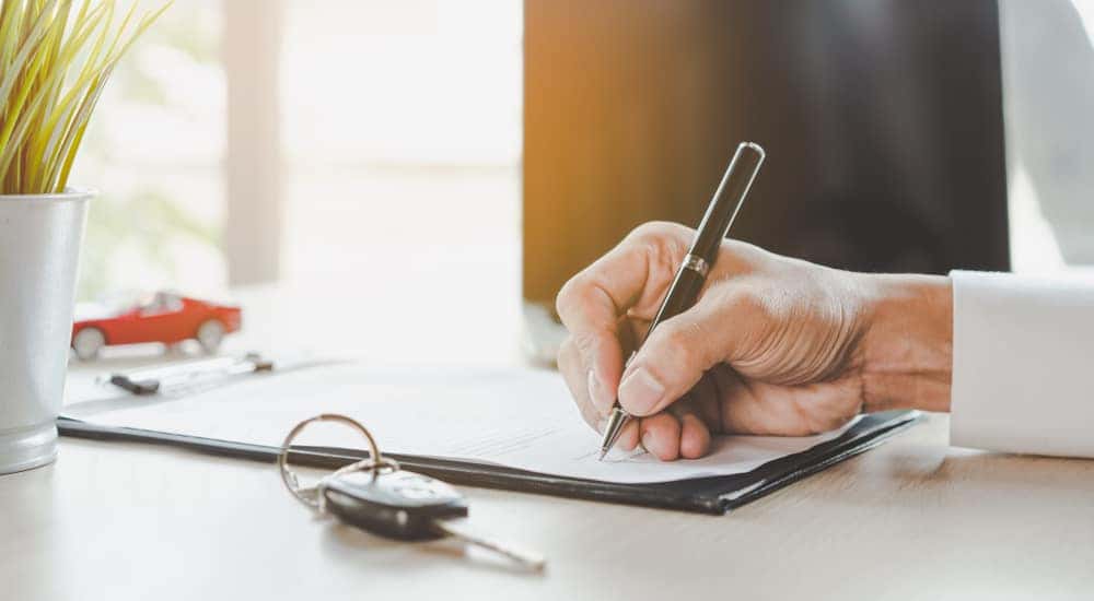 Hand holding a pen and signing a car lease with car keys next to it