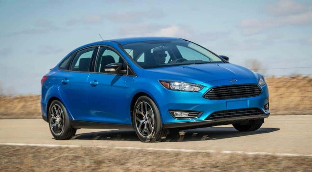 A blue 2018 Ford Focus is driving on a grass lined during the sunny day.