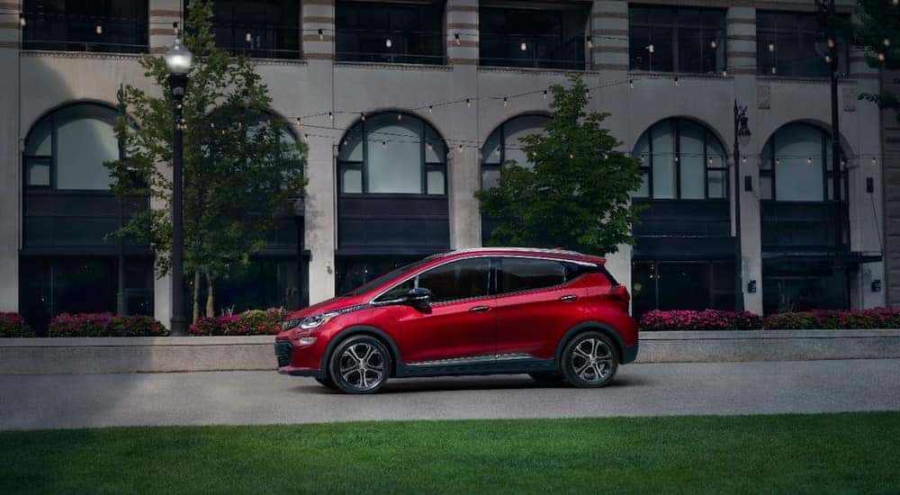 Red 2020 Chevrolet Bolt EV parked in front of a stone building with large windows and trees