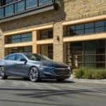 Grey 2020 Chevrolet Malibu sedan parked in front of a brick building with large windows