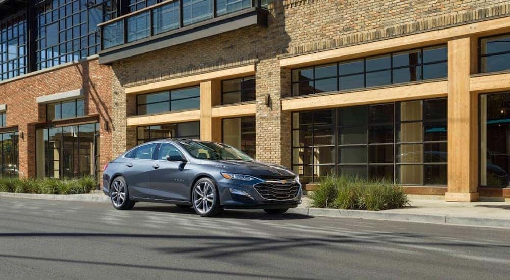 Grey 2020 Chevrolet Malibu sedan parked in front of a brick building with large windows