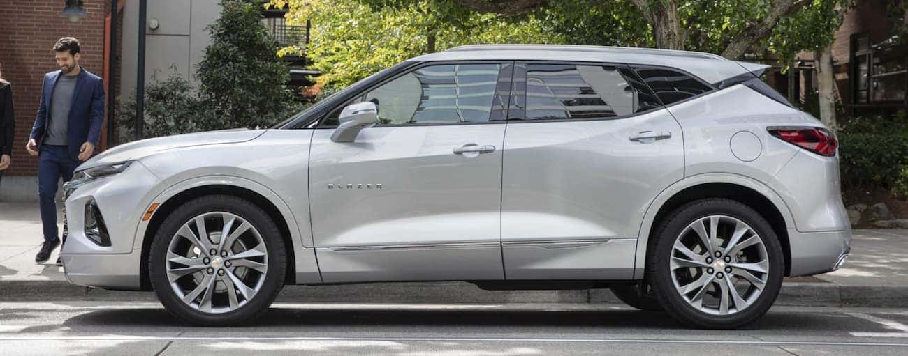 A side view of a silver 2020 Chevy Blazer is parked on the side of a treelined street.