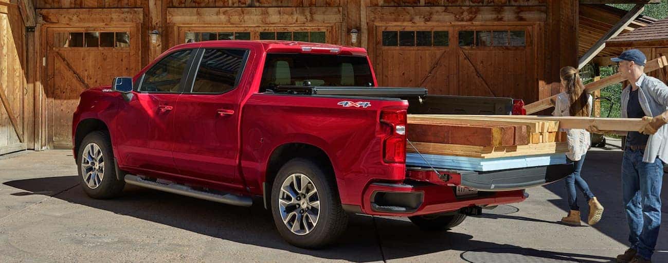 A couple is loading heavy pieces of wood into the bed of their red 2020 Chevy Silverado 1500.