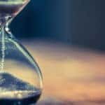 Sand falling through a clear glass hourglass sitting on a wooden table