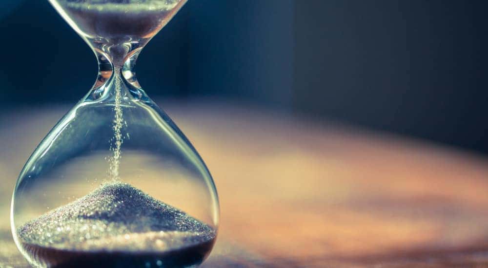 Sand falling through a clear glass hourglass sitting on a wooden table