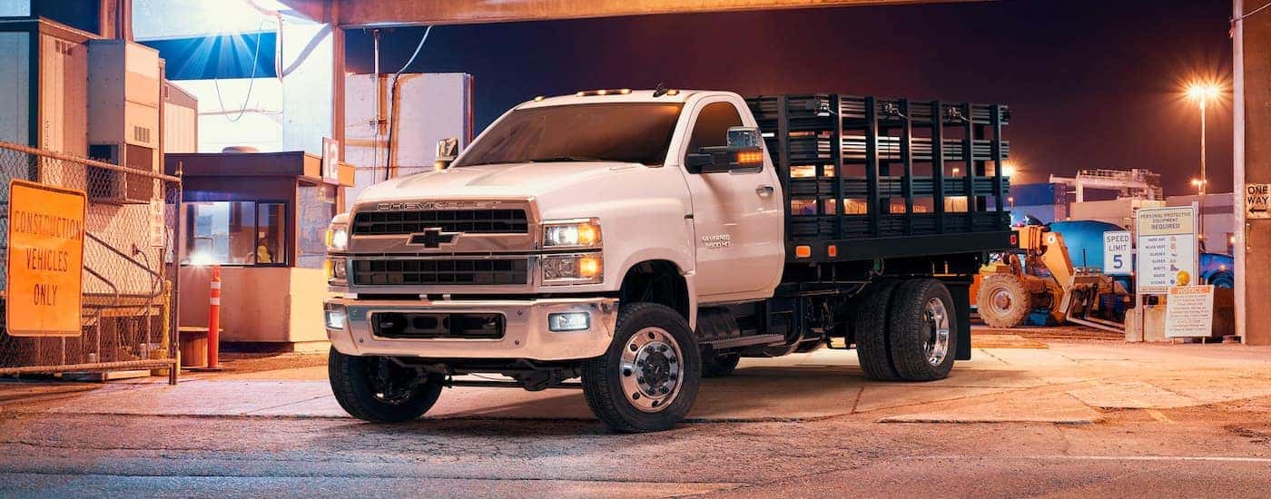 A white 2021 Chevy Silverado 5500 HD is shown from the front, angled left, in a shipping yard.