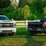 Two 2020 Chevy Silverado HD's, a whiote 2500 and a black 3500 dually, are parked on grass at a farm.