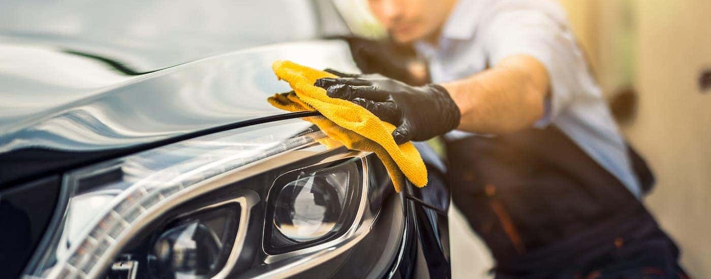 A car detailer is rubbing a cloth on a black car near Clifton Park, NY.