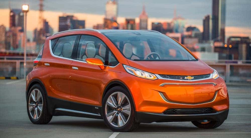 Orange 2015 Chevrolet Bolt EV hatchback parked on cement in front of tall city buildings