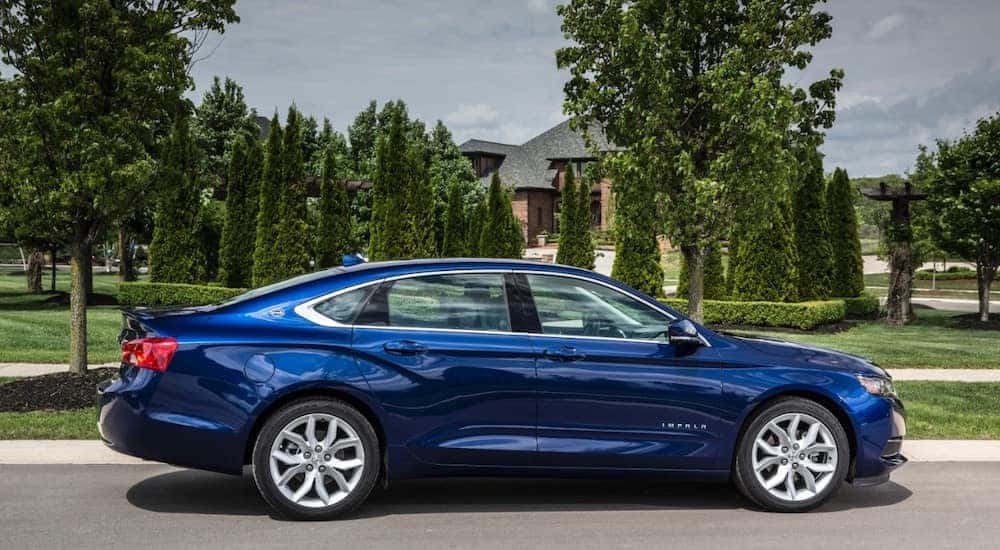 Blue 2016 Chevrolet Impala sedan parked in front of a house with a green lawn and trees out front