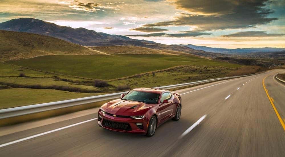 Red 2017 Chevrolet Camaro driving on a paved road next to a guard rail with mountains in the distance
