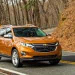 Orange 2019 Chevrolet Equinox SUV driving down a paved road next to trees and a hill